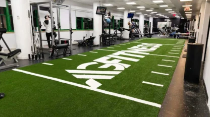A gym interior with a turf area labeled "Fitness," weightlifting equipment, and exercise machines. People are working out in the background.