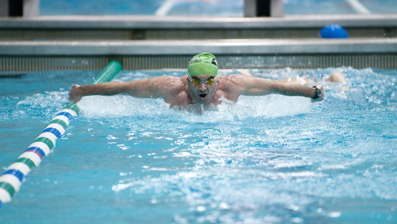 A swimmer wearing a green cap and goggles competes in a pool, performing the butterfly stroke.
