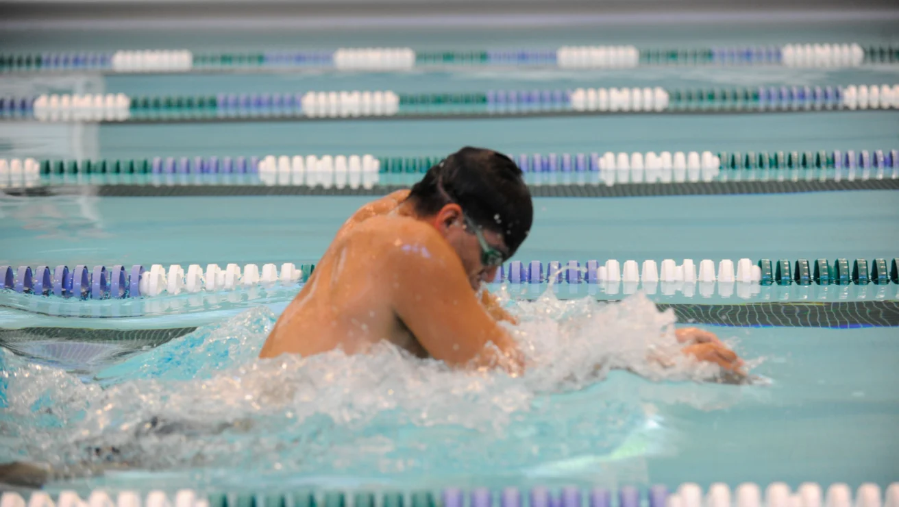 A swimmer wearing goggles performs a breaststroke in a lane of a swimming pool.