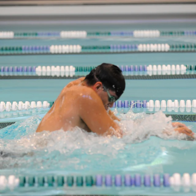 A swimmer wearing goggles performs a breaststroke in a lane of a swimming pool.