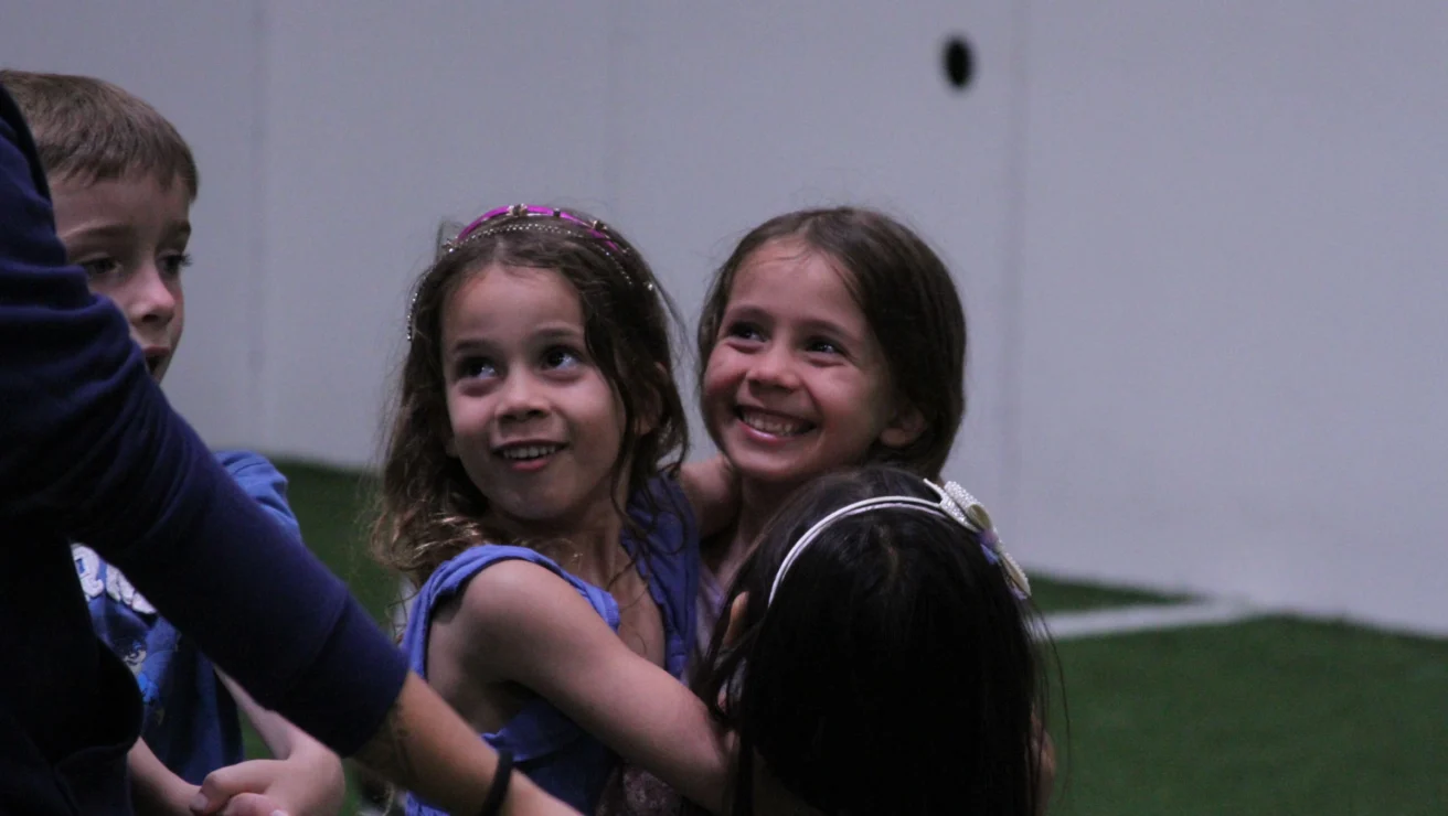 Children playing and hugging on a green indoor field.