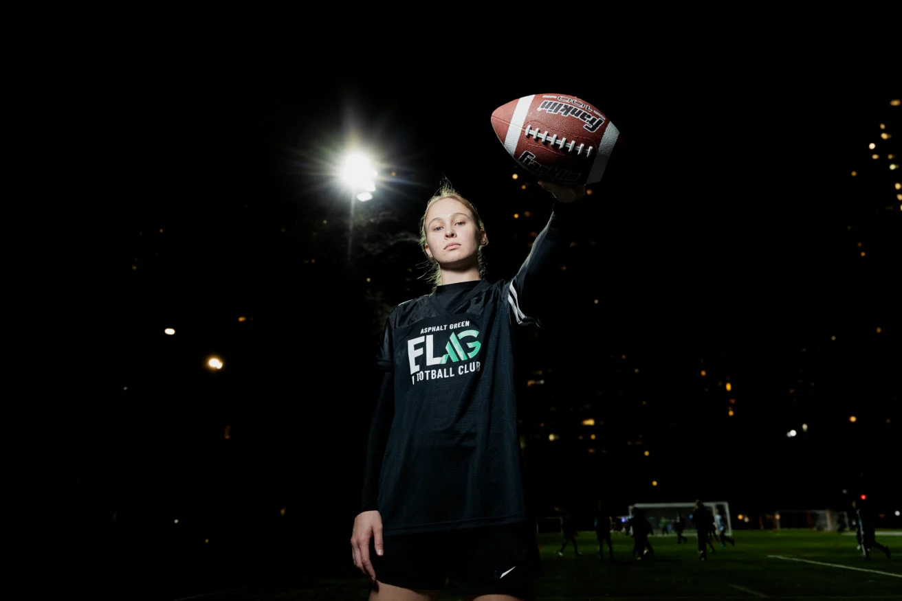 A person in a sports uniform holds a football aloft on a lit field at night.