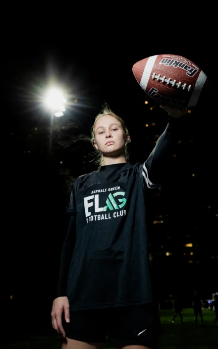 A person in a sports uniform holds a football aloft on a lit field at night.