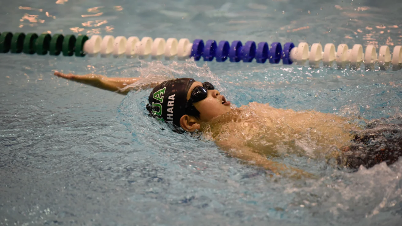 A swimmer performs the backstroke in a pool, wearing goggles and a swim cap, near the lane divider.