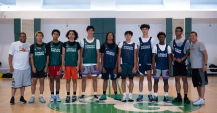 A group of ten basketball players, wearing jerseys, pose on an indoor court with two coaches standing beside them.