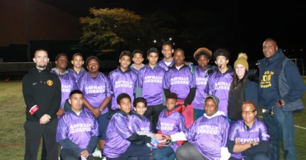 A group of people wearing matching purple jerseys poses for a photo on a field at night.