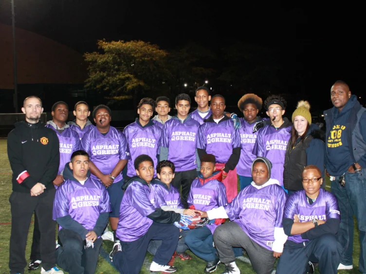 A group of people wearing matching purple jerseys poses for a photo on a field at night.
