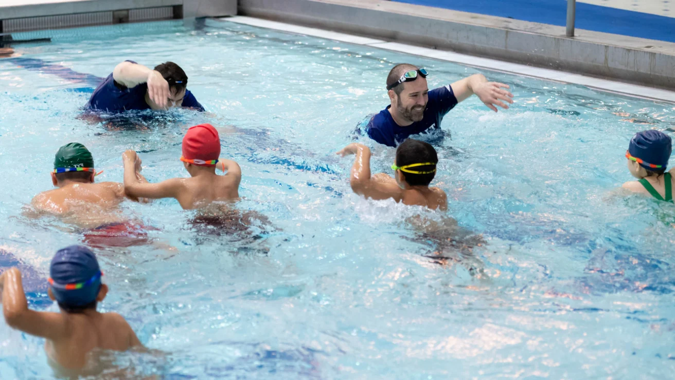 Swimming instructors guide a group of children in a pool during a swim lesson.