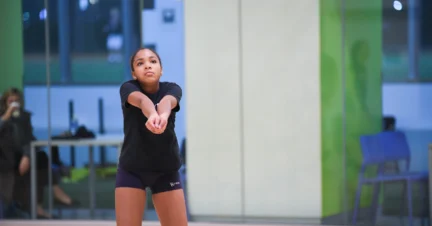 A person in sports attire prepares to hit a volleyball in an indoor gymnasium.