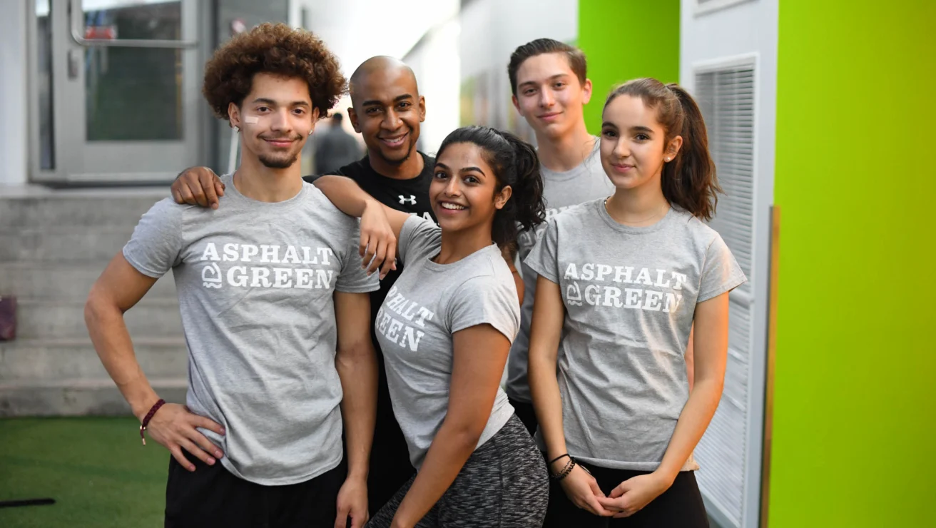 Five people wearing "Asphalt Green" shirts pose together indoors.