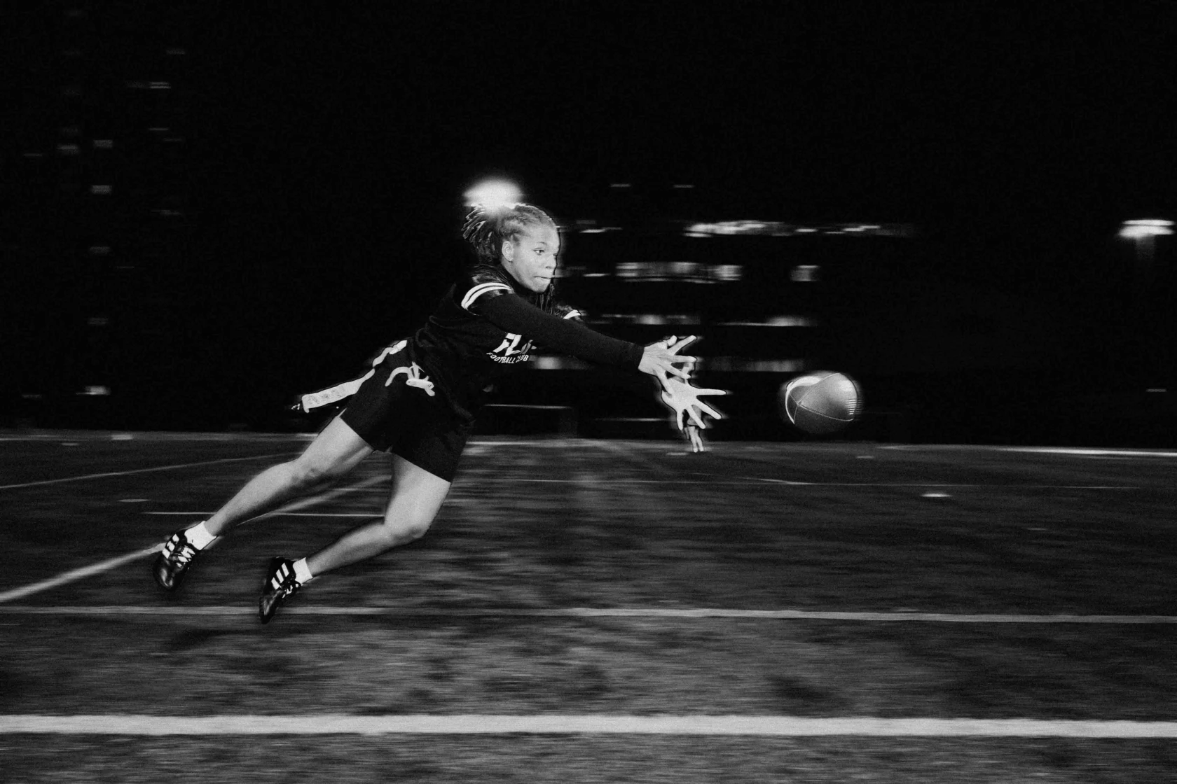 A person in athletic gear dives to catch a football on a field at night.