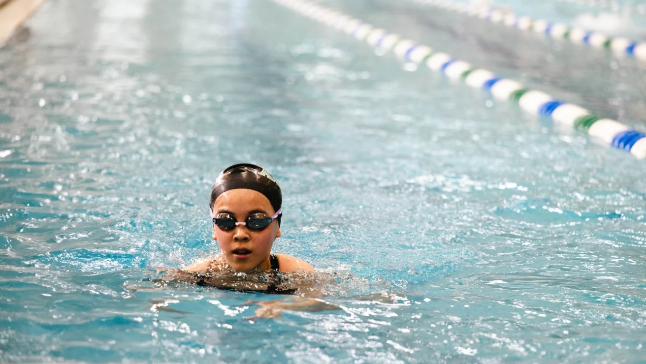 Swimmer wearing goggles and a swim cap competes in a lap pool, surrounded by lane dividers.