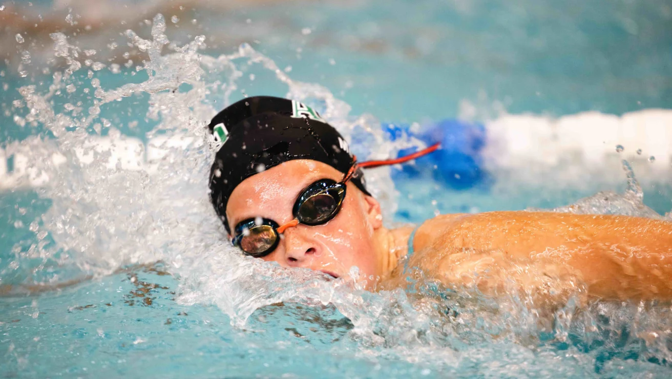 A swimmer wearing goggles and a swim cap competes in a pool, creating splashes as they move through the water.