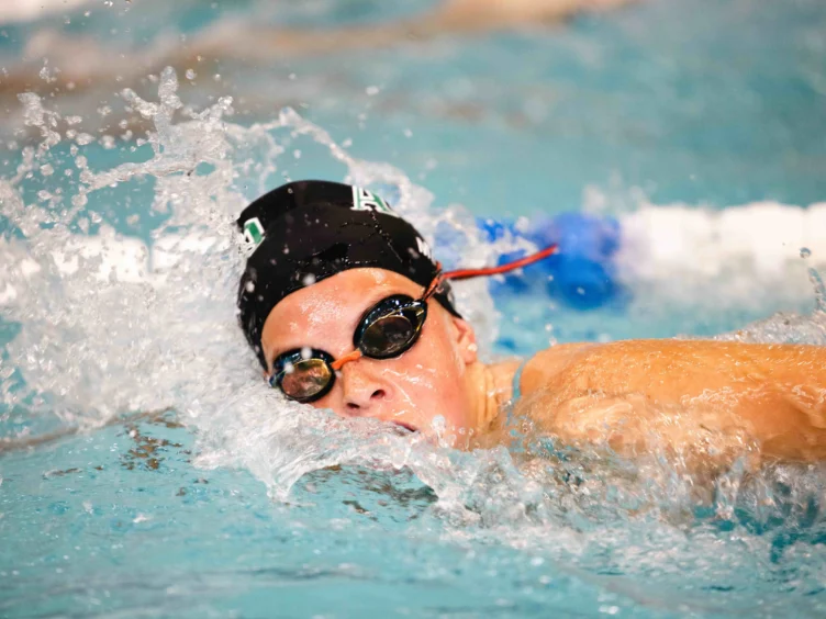 A swimmer wearing goggles and a swim cap competes in a pool, creating splashes as they move through the water.