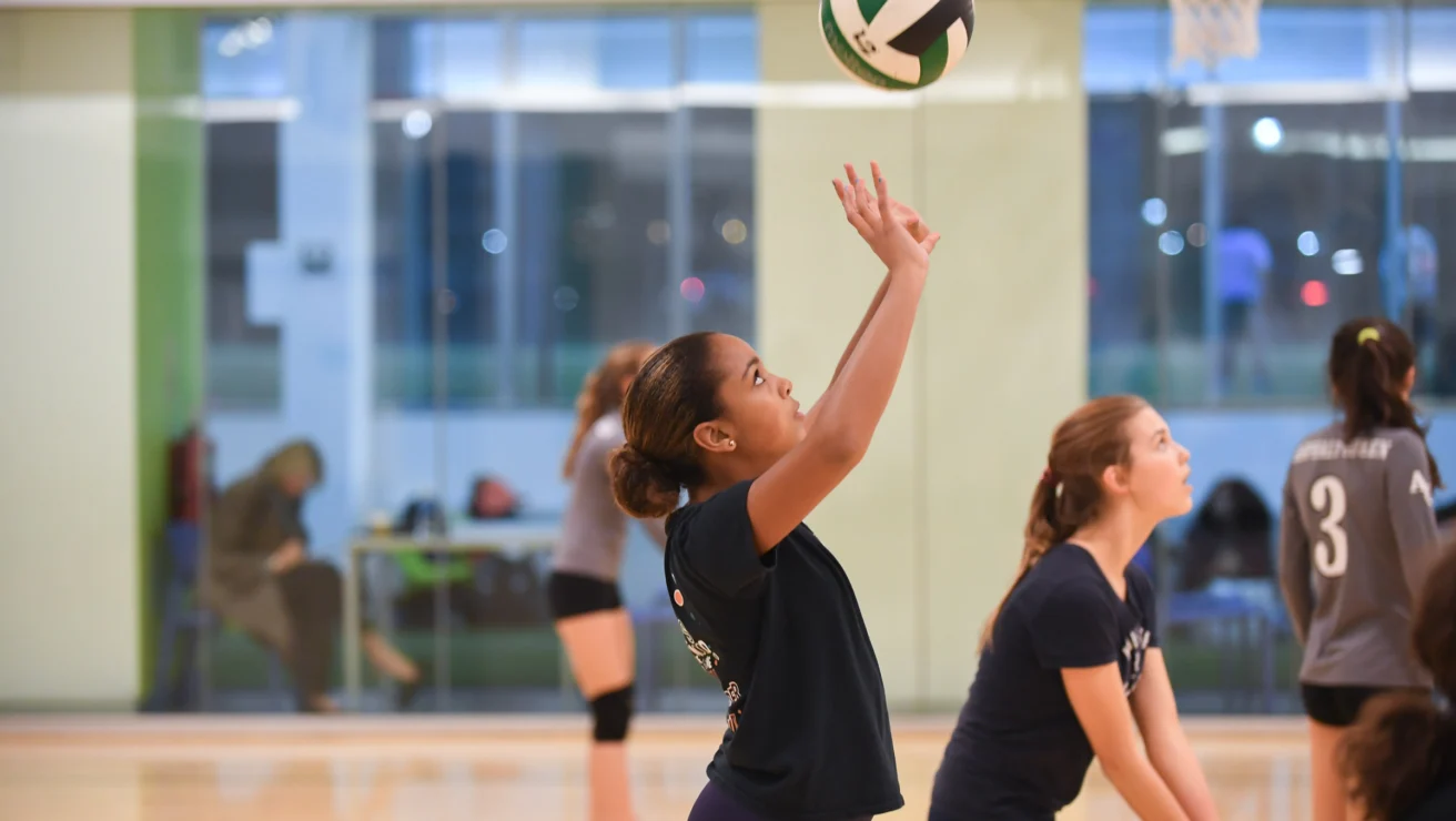 A volleyball player prepares to hit the ball indoors while teammates and opponents watch.