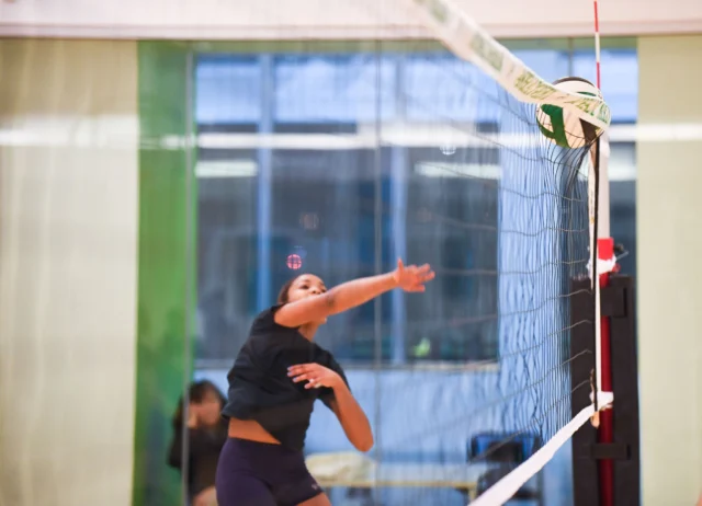 A volleyball player in mid-air prepares to hit the ball over the net during an indoor game.